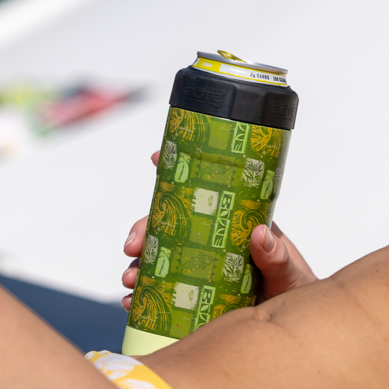 Hand holding Native Nalu can cooler with green and yellow pattern outdoors.