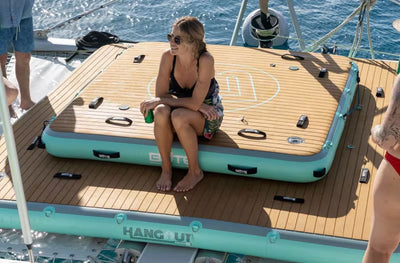 Woman sitting on a Hangout Dock 7 stacked on top of a Hangout Dock 10 inflatable platform on top of a boat with water in the background