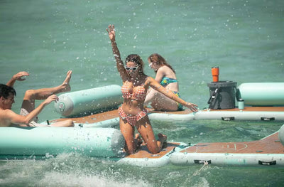 A woman in a polka dot bikini and sunglasses enjoys splashing in the water on a Hangout Couch.