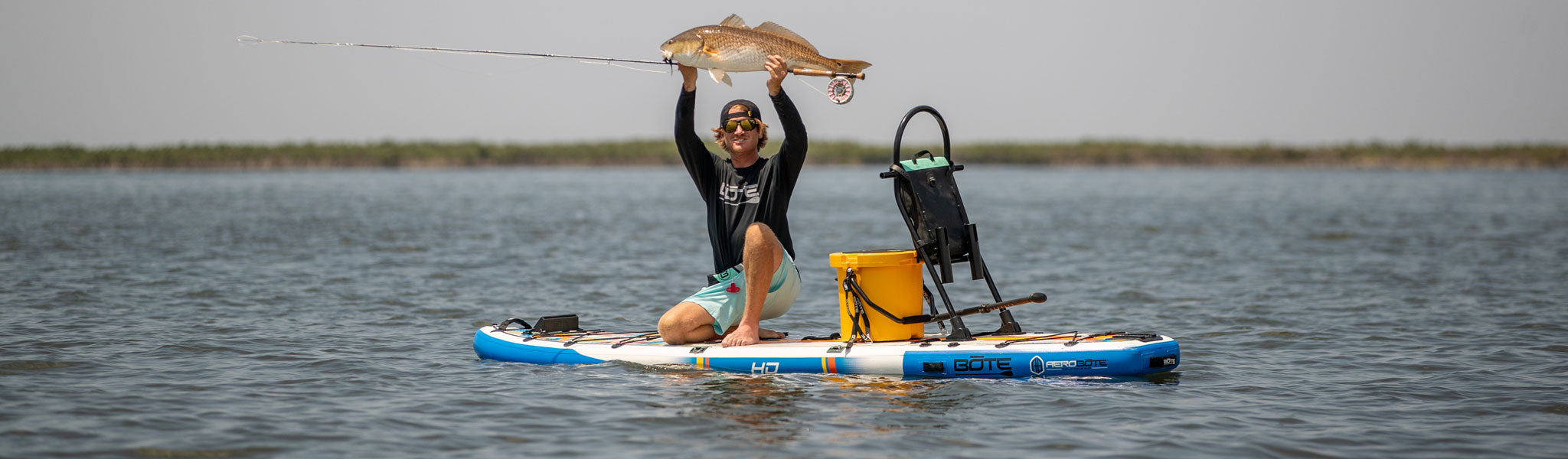 A guy holding up a redfish while on a HD Aero inflatable paddle board