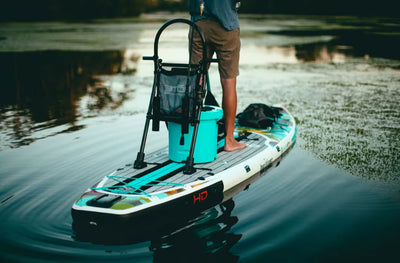 Person on a paddleboard with a paddle and cooler on a calm body of water