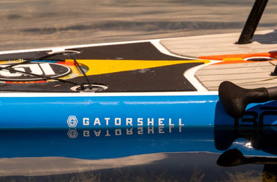Close-up of the blue HD Gatorshell paddle board edge with logo reflecting on the water.
