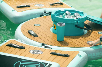 Inflatable KULA bar and additional platforms on water, featuring teal coolers filled with canned beverages.