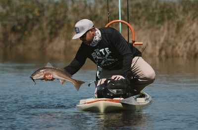 Man pulling a fish from the water while kneeling on the Rackham GS.