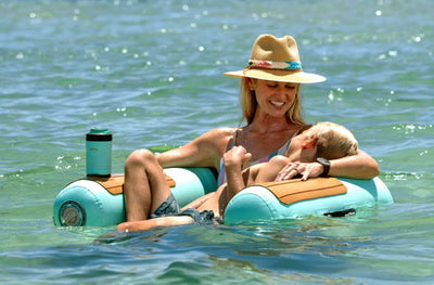 Woman wearing a straw had holds a child while lounging in the Inflatable Hangout Sling Chair.