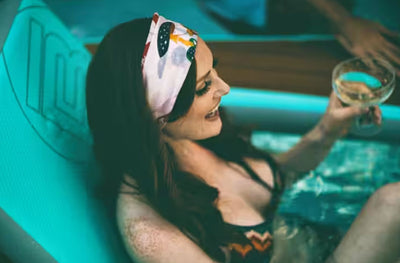 Woman smiles while holding a drink while seated in the Inflatable Hangout Sling Chair.