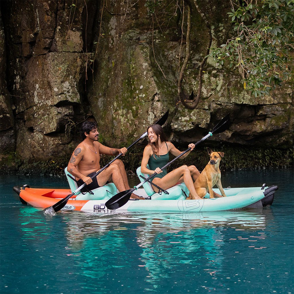 A guy, girl and dog paddling a Zeppelin Aero 12′6″ Classic Seafoam Inflatable Kayak on the water