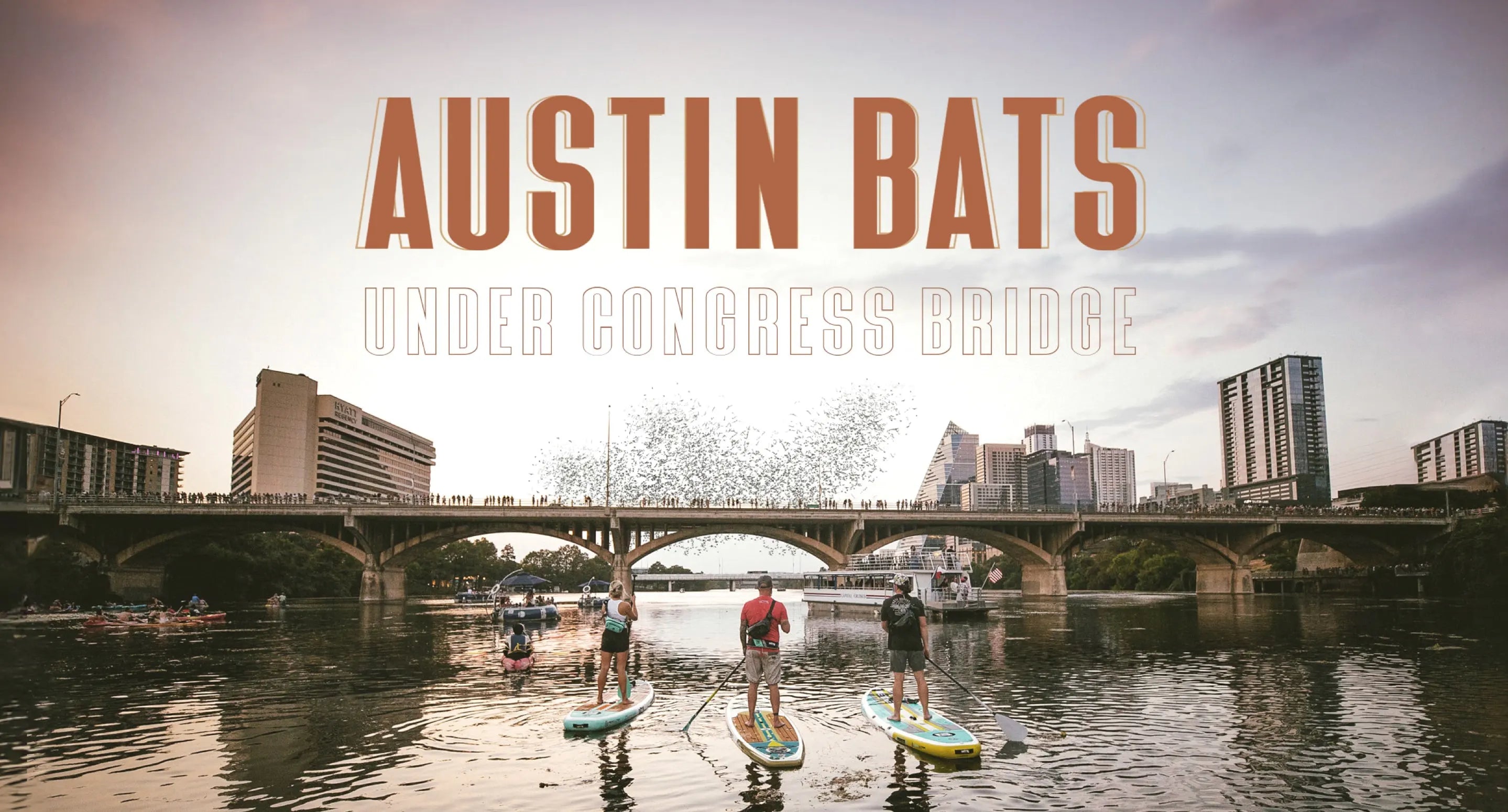 Three people paddleboarding towards the Congress bridge preparring to see bats fly out from underneath with the words " AUSTIN BATS- Under Congress Bridge."