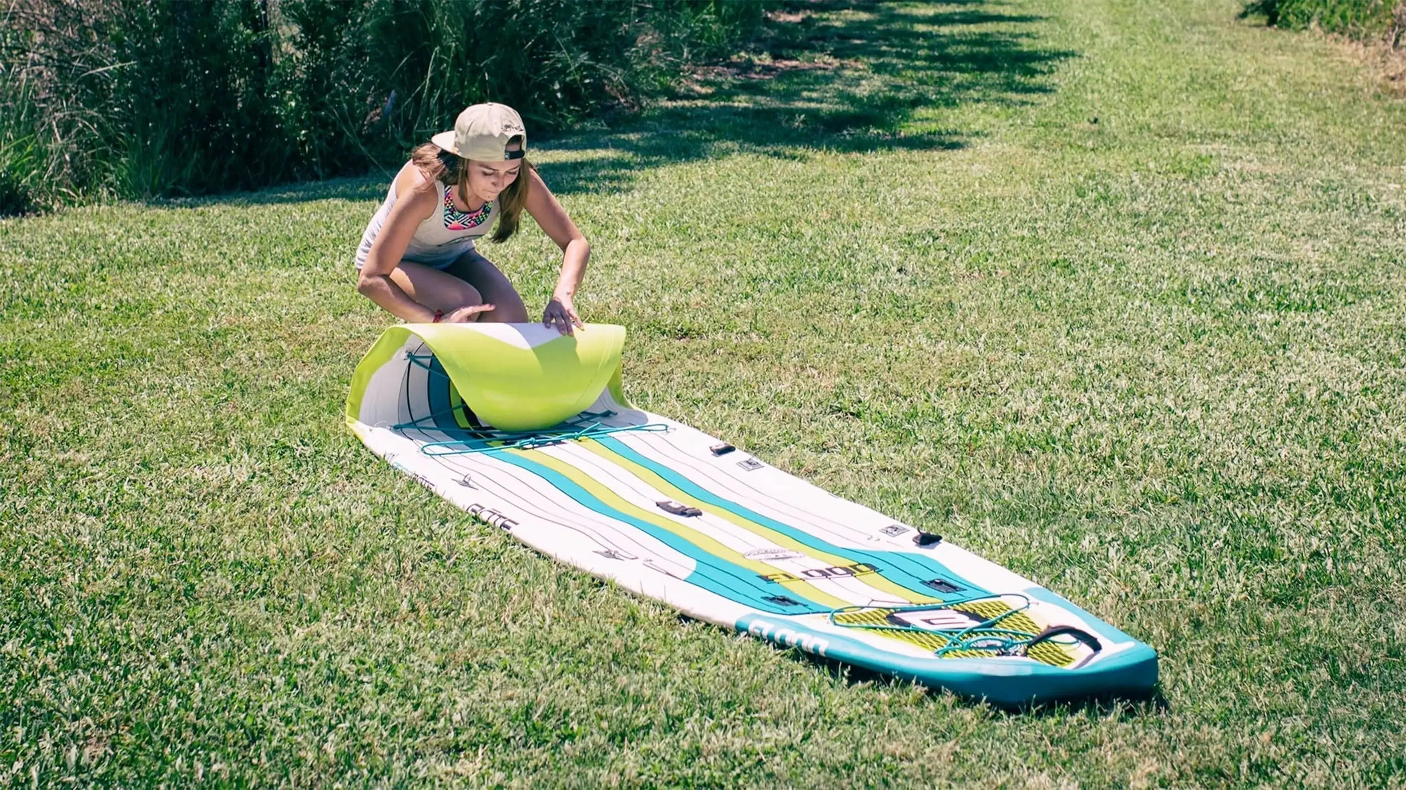 Woman rolling up her inflatable paddleboard for easy travel sitting on grass.
