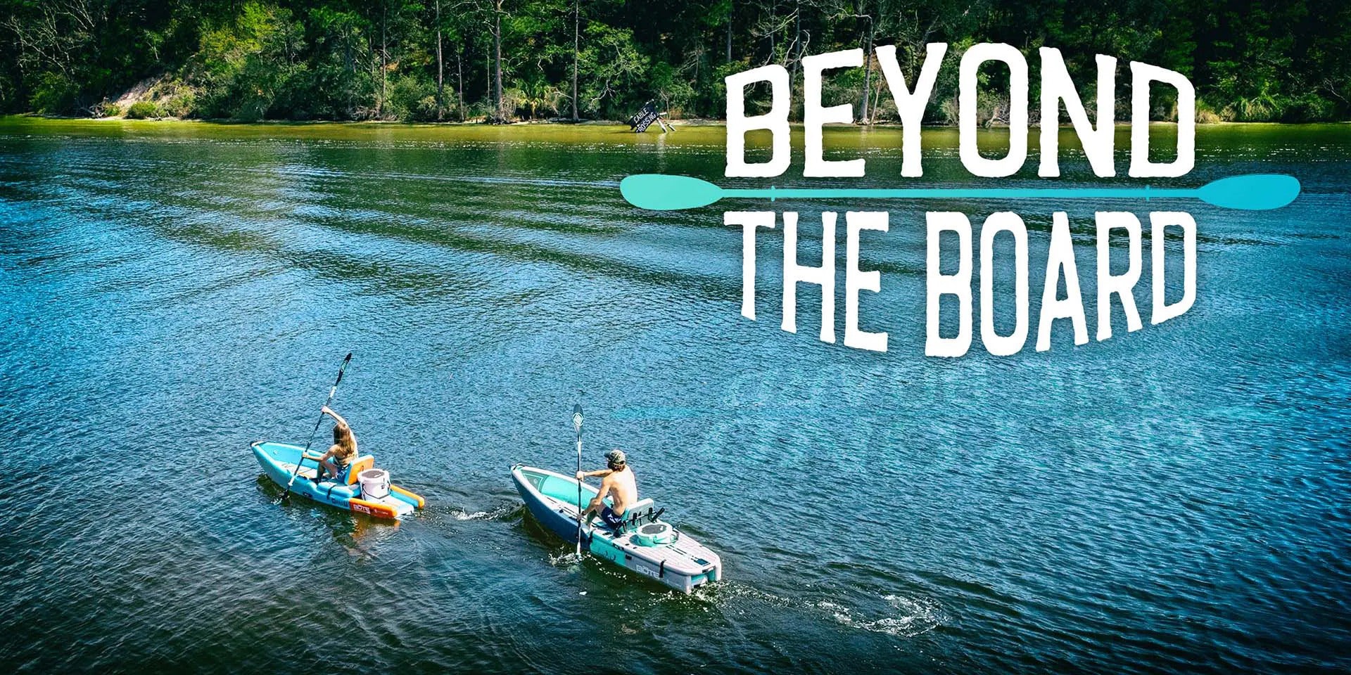 Arial view of two paddlers on inflatable kayaks on calm water with trees on the shoreline.