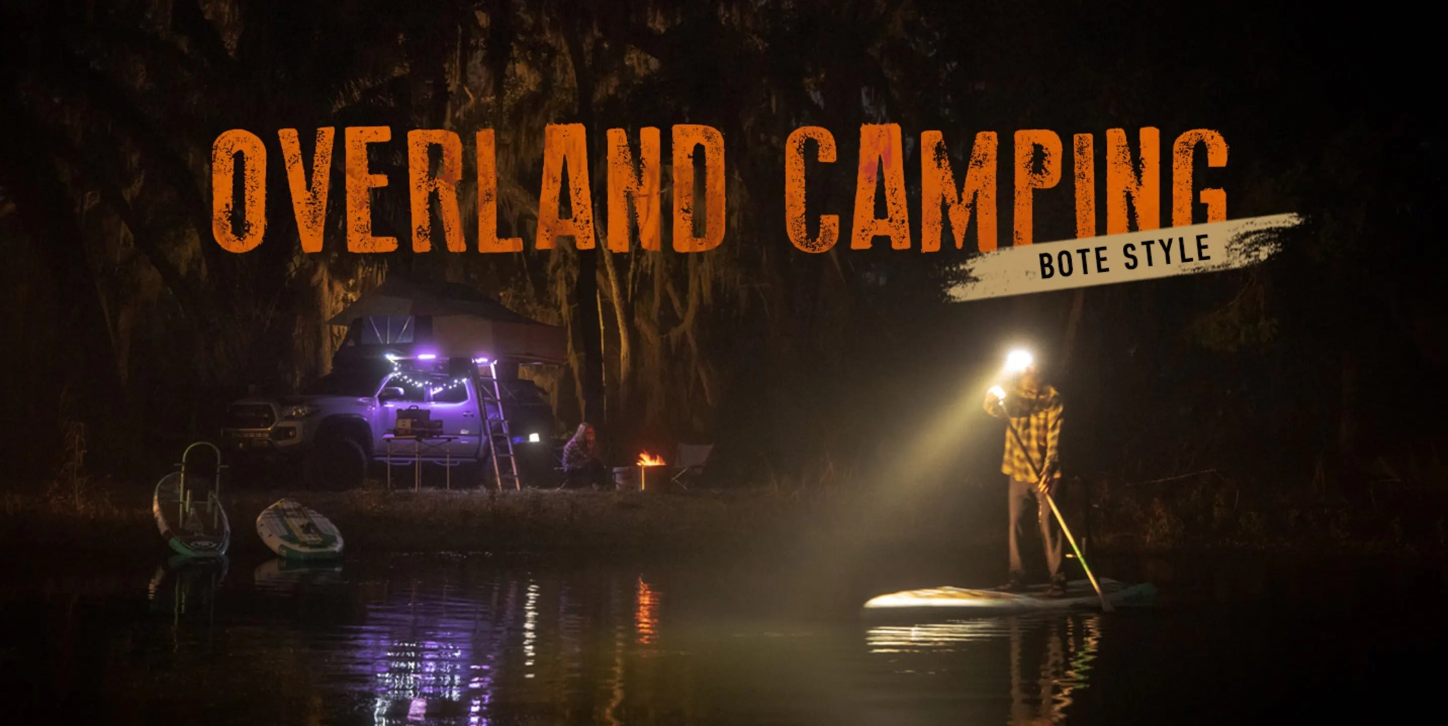 Paddle boarder on calm water at night with a head lamp paddling past his truck camping spots that has purple lights shining in the background. Text overlay saying "Overland camping BOTE Style"