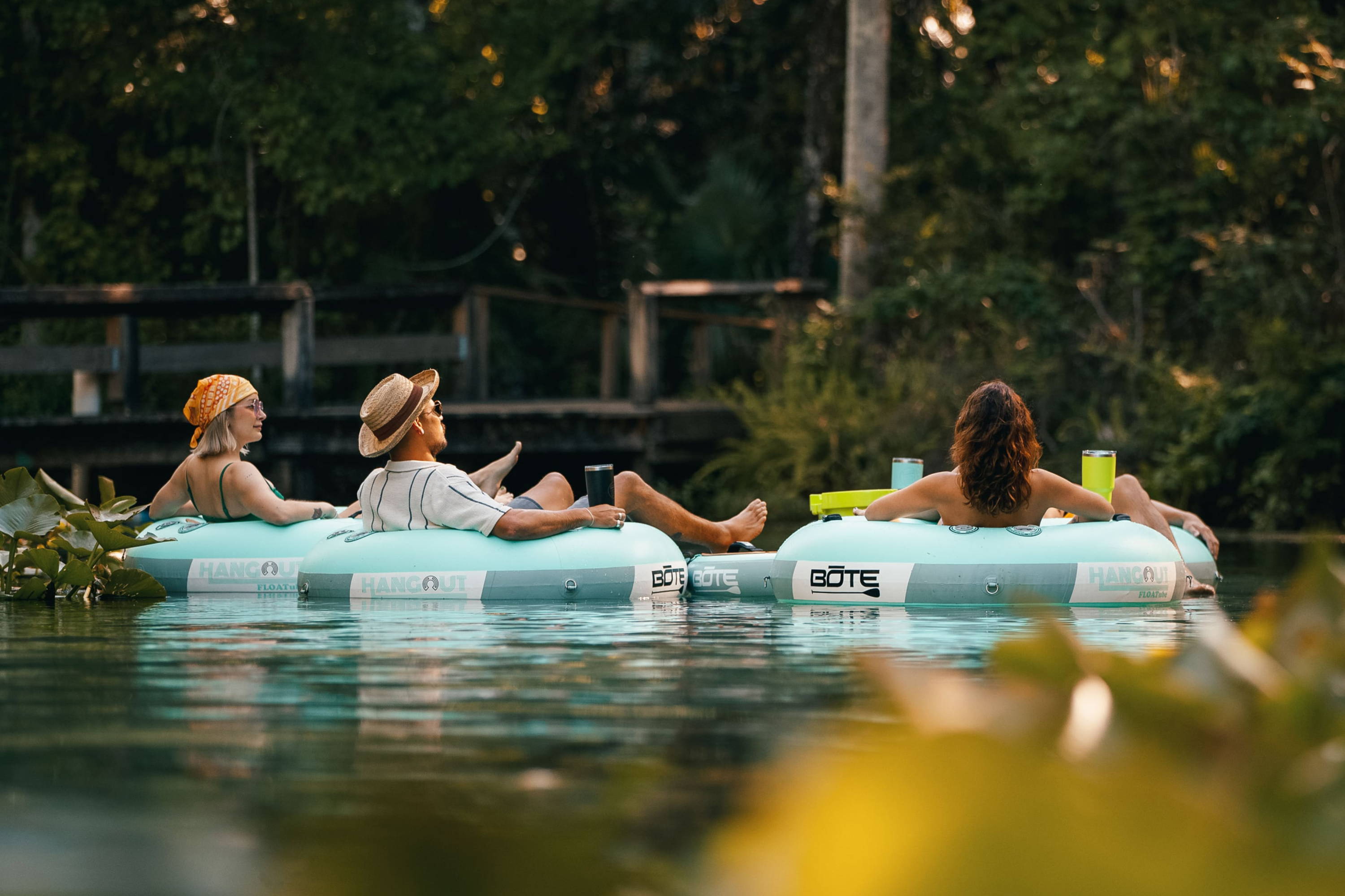3 peopple lounging on their BOTE Tubes enjoying some drinks on calm water.