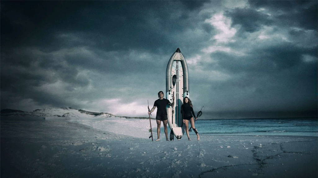 Two people walking on a stormy beach carrying paddles beside an upright kayak.