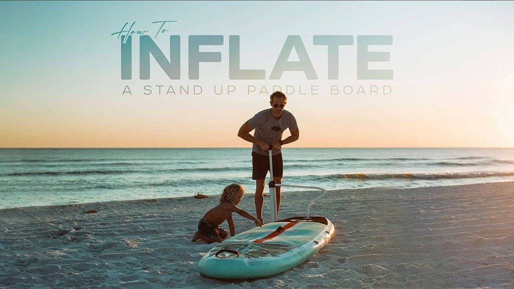 A guy pumping up an inflatable paddle board at the beach