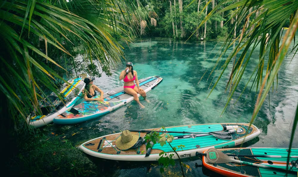 Two people paddleboarding in a clear, tropical lagoon surrounded by greenery.