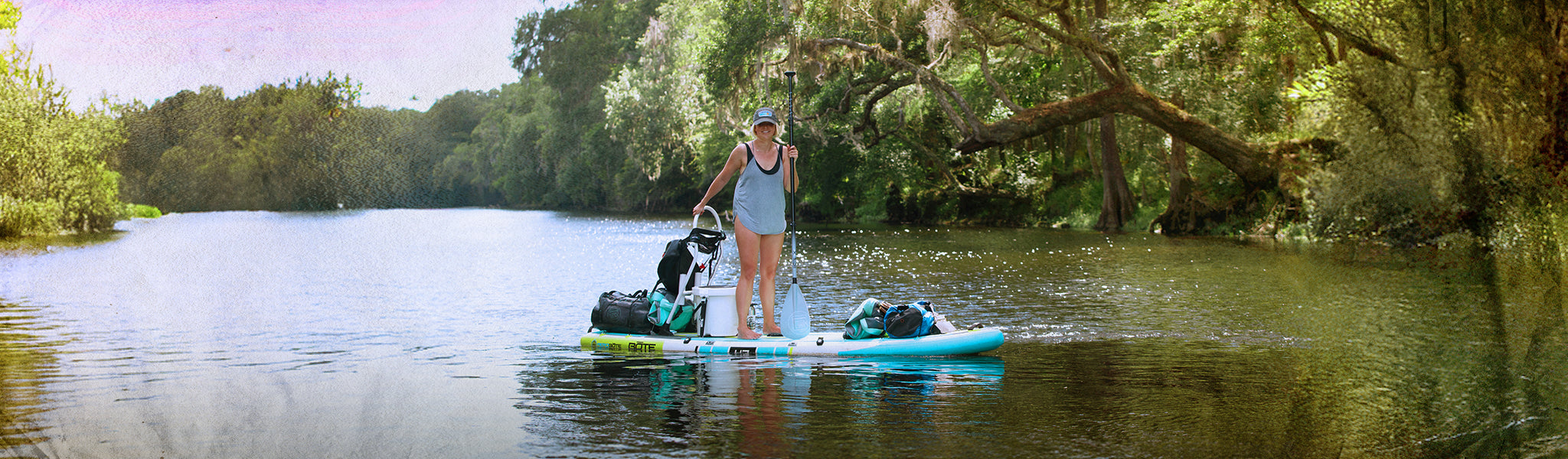 Person on a stand-up paddleboard in a river surrounded by trees