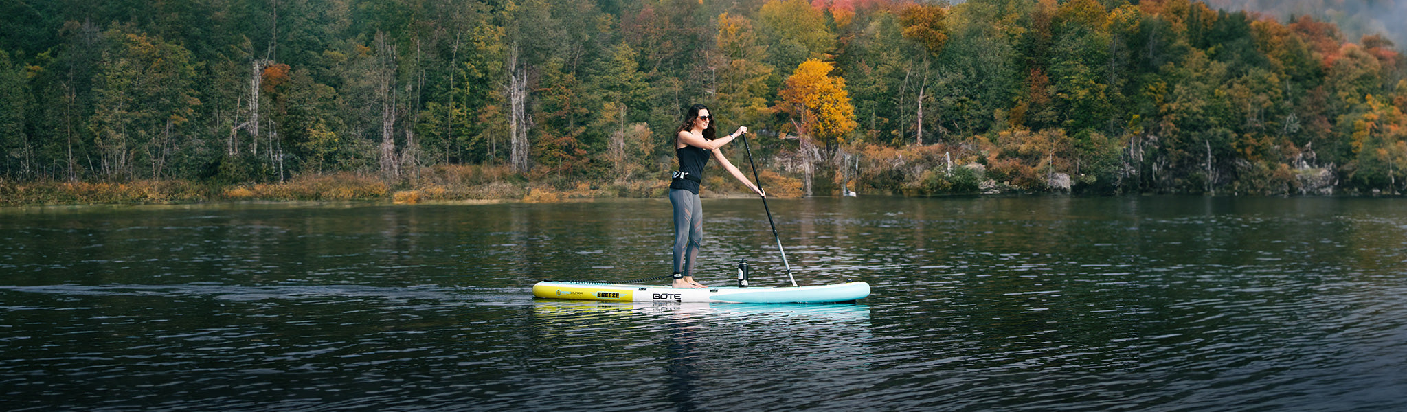 Person paddleboarding on a lake with trees in the background