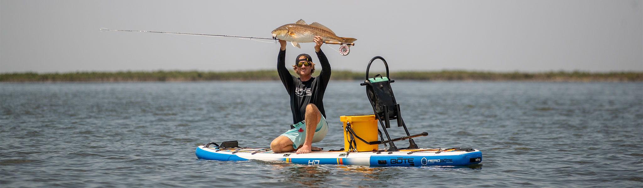 A guy holding up a redfish on a HD Aero Inflatable Paddle Board