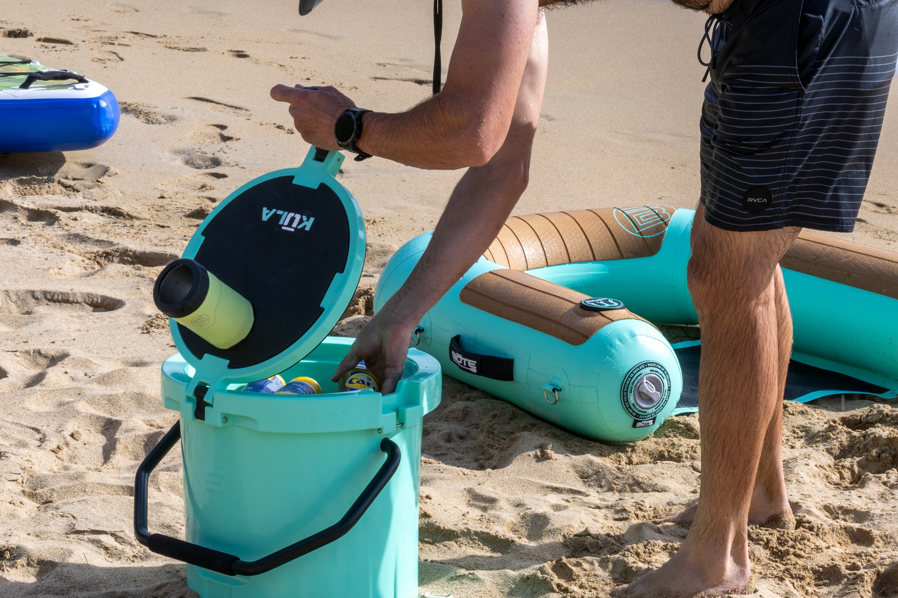A person grabbing a drink out of a turquoise cooler.