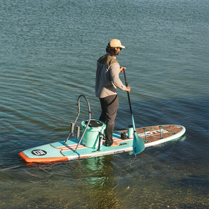 Man standing on a Breeze Gatorshell paddleboard with a cooler and RAC system on calm water.