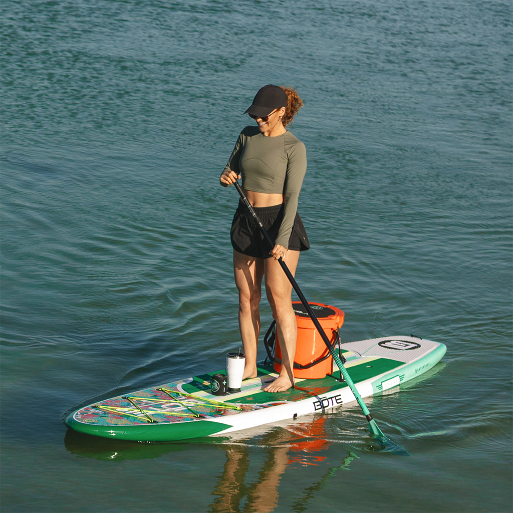 Woman paddleboarding on a Breeze Gatorshell with a cooler and tumbler on calm water.