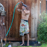 Man spraying hose on himself while wearing a towel around his waist
