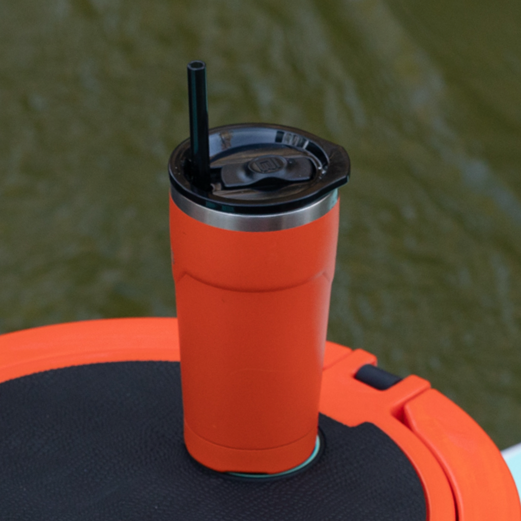 MAGNETumbler 20oz with Lid Sunrise shown upright with straw on a black deck pad over water.