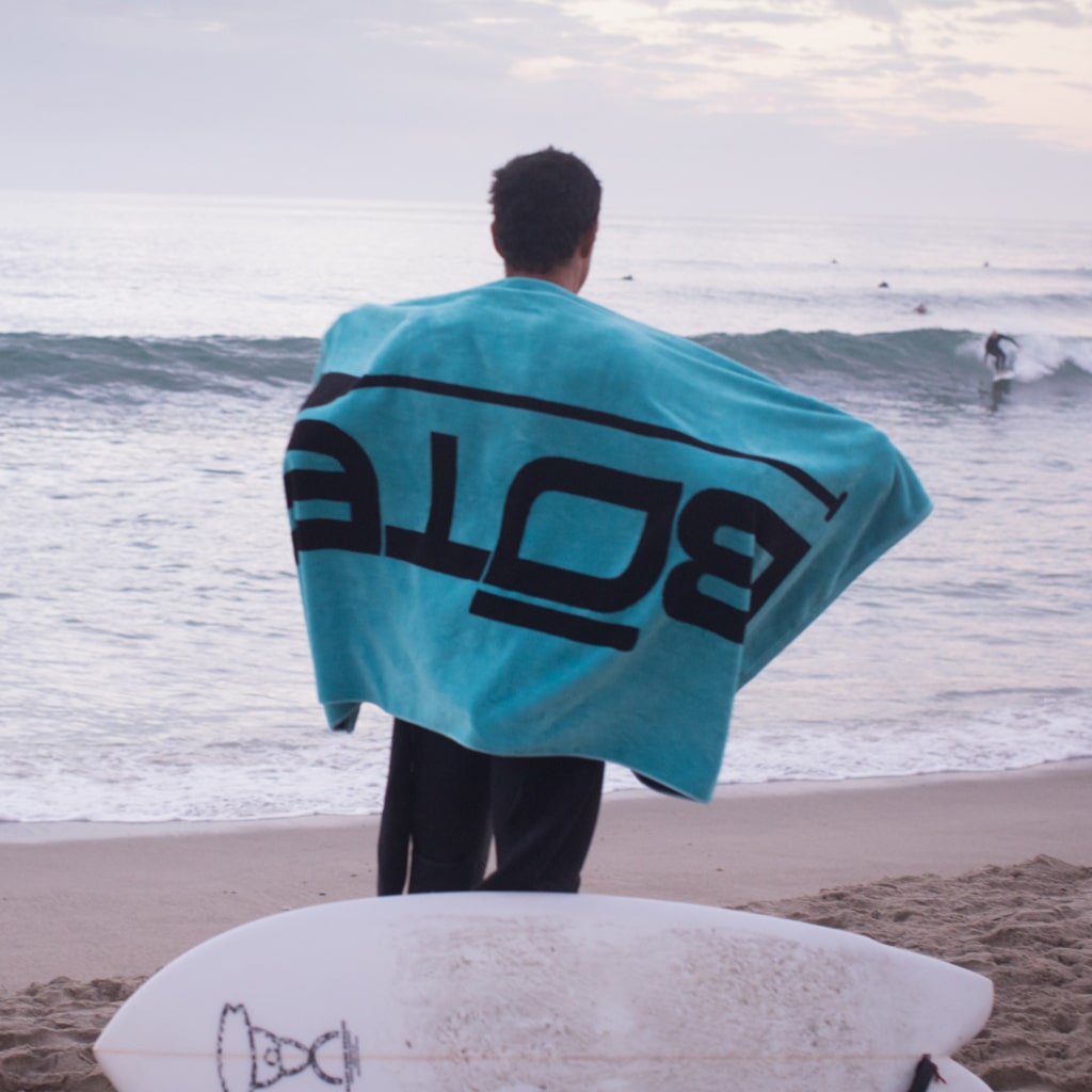 Man with BOTE logo towel over his shoulders at the beach