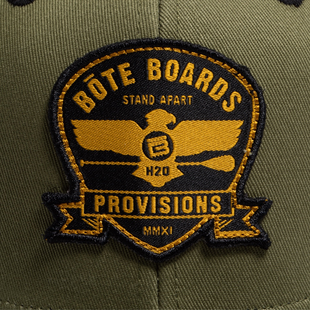 Closeup on the patch of Eagle Supply Trucker Hat in Green with black and yellow logo with eagle holding a paddle.