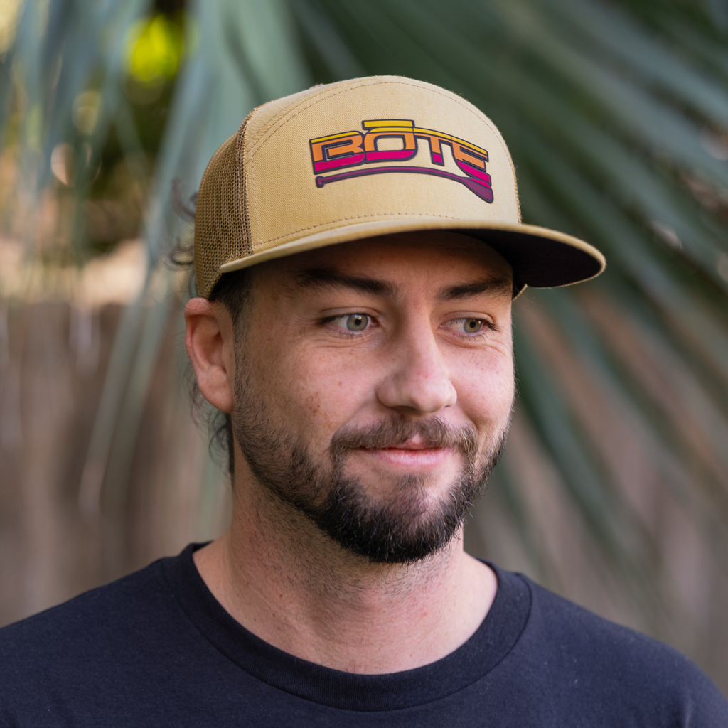 Front view of person wearing the BOTE Desert Logo 7 Panel Hat in Yellow. Featuring a yellow, orange, and red BOTE logo.