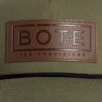 Closeup of brown leather patch on a green BOTE Boxed Logo Hat .