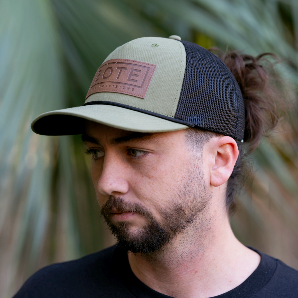 Front view person wearing the green BOTE Boxed Logo Hat with brown Patch logo and black mesh back.