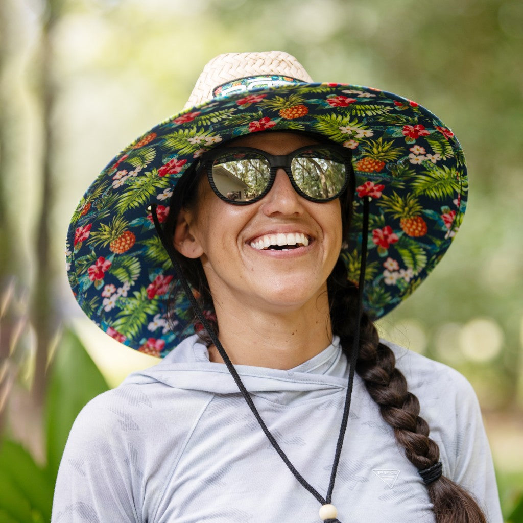 Person smiling wearing the BOTE Native Cuda Straw Hat with Hawaiian print design on the underside of the brim and a black drawstring.