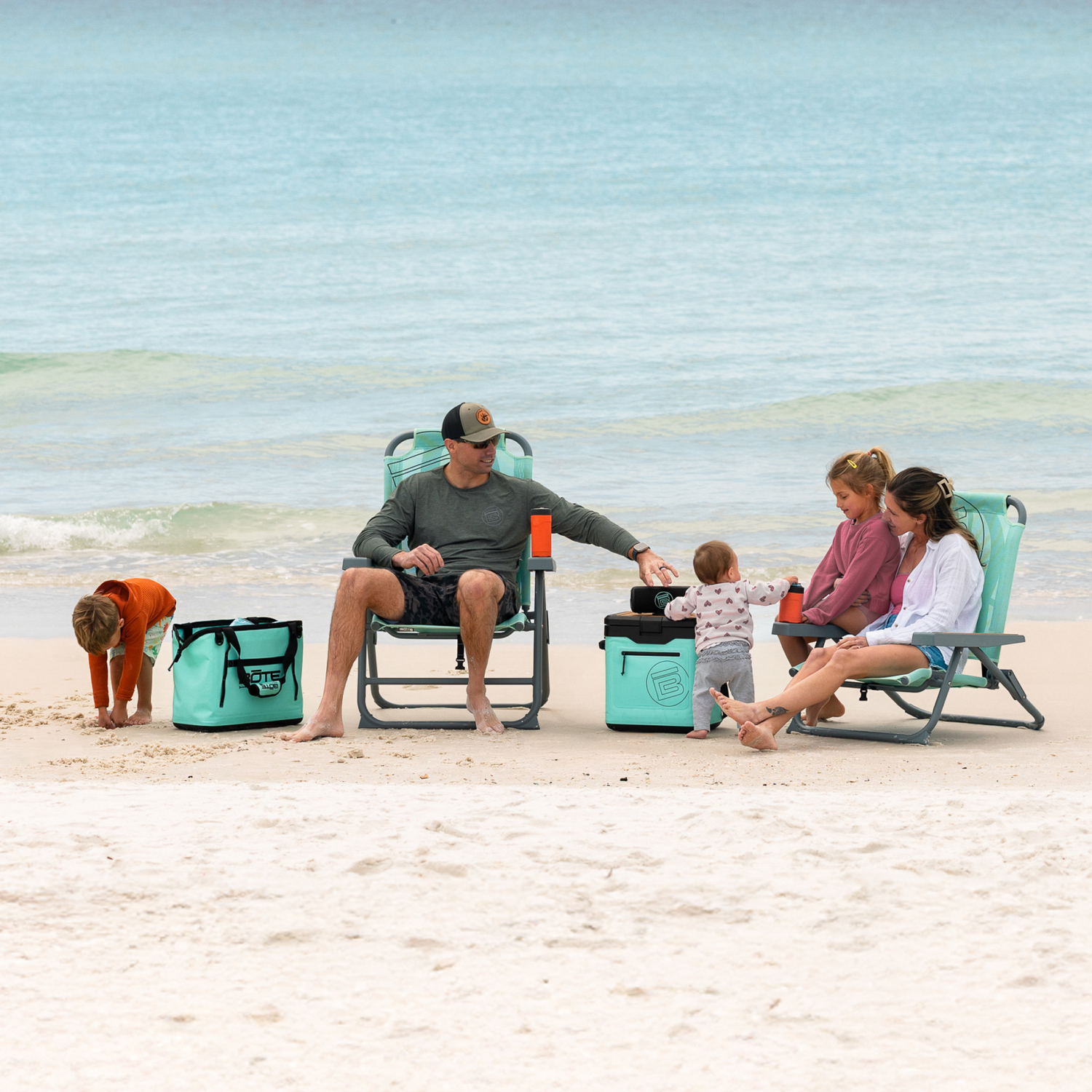 Wide lifestyle view of family using Mule Series Full Haul chairs, tote, and cooler on beach.