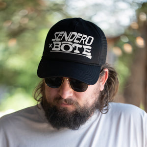 An image of man wearing BOTE Sendero Trucker Hat in Black with a white BOTE x Sendero logo.