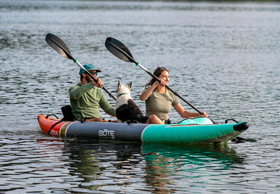 Two paddlers and a dog on the Koda Aero Tandem glide across calm water.