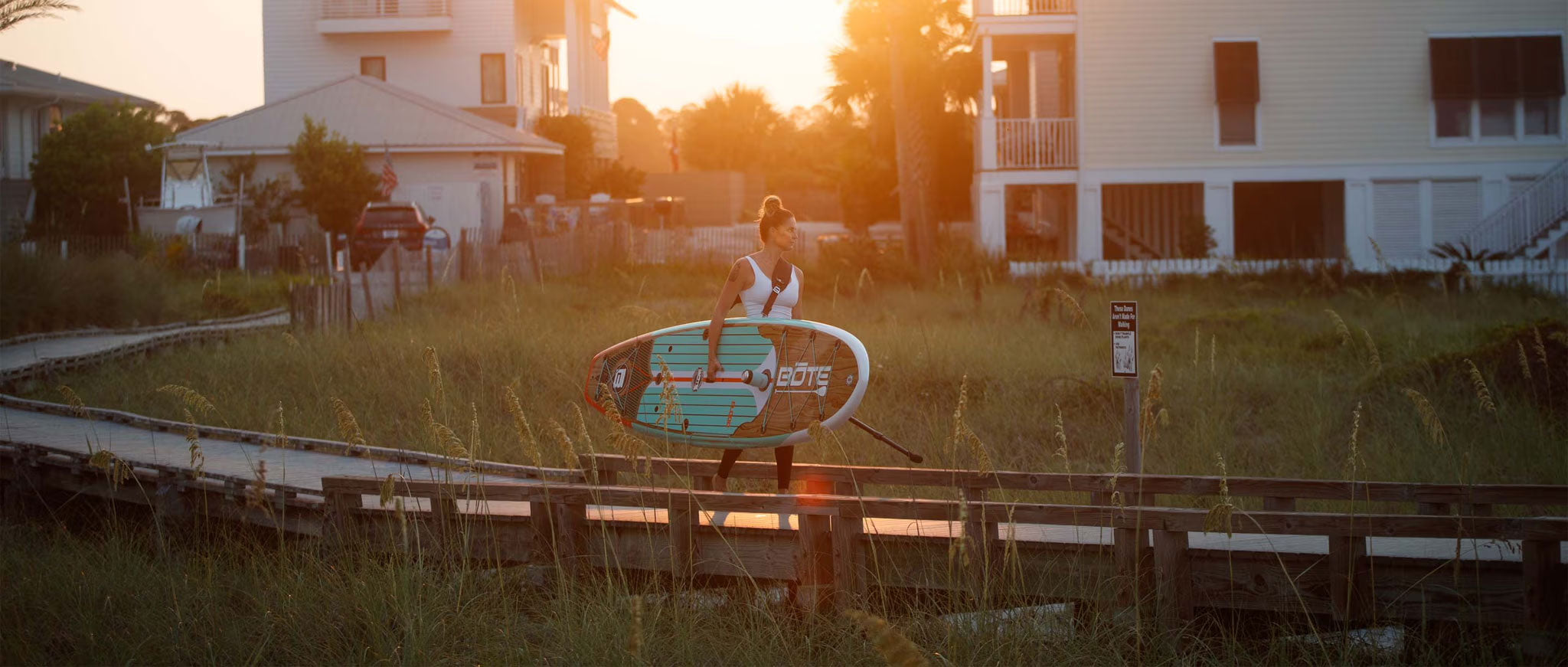 Woman walking a paddleboard with a sign in the foreground at sunset.