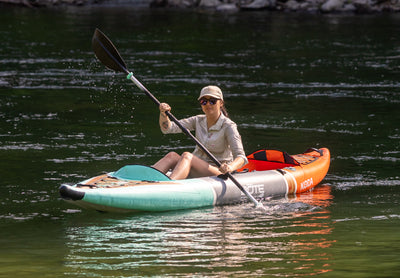 Angled view of a paddler cruising the Koda Aero on a river with wide inflatable hull.