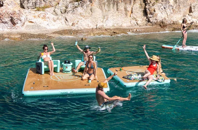 Multiple people enjoying time floating on water on the Hangout 10 with another Hangout 7 attached. One swimmer jumping off the dock while a paddleboarder floats buy in the background.