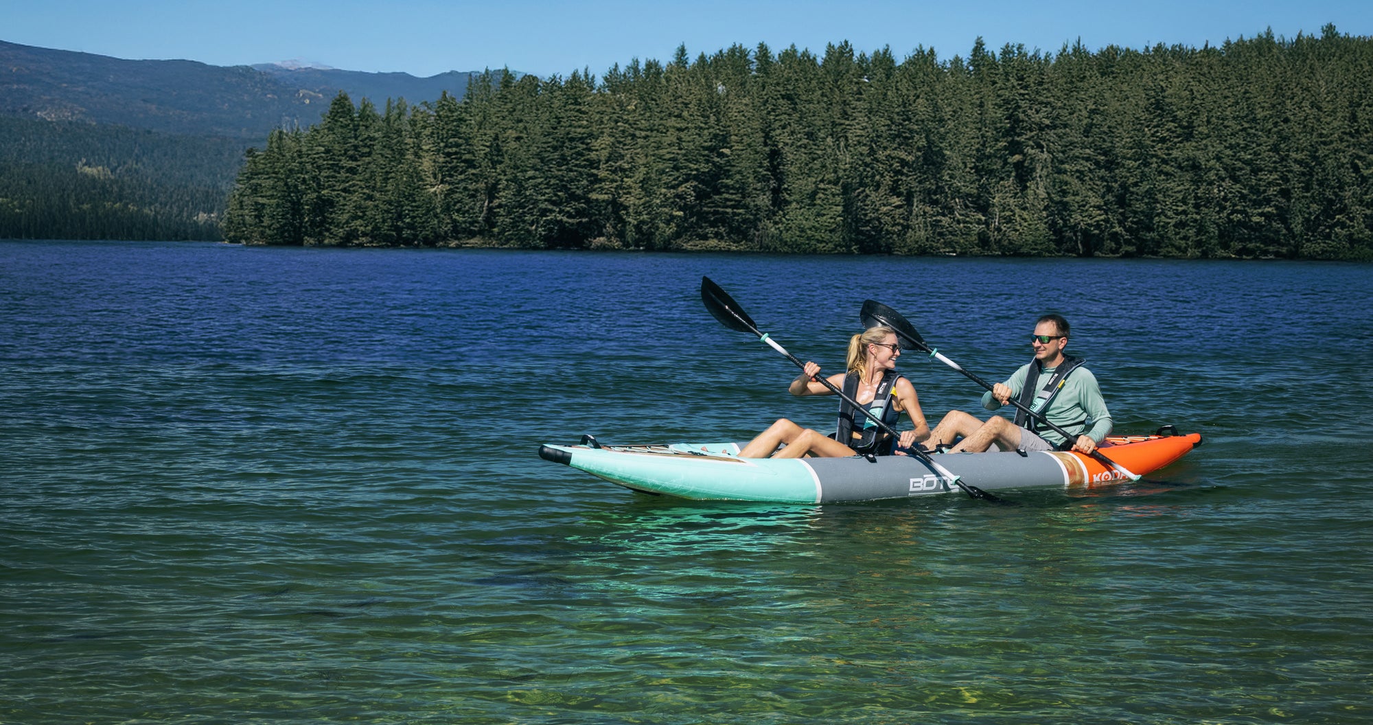 Koda Aero tandem setup with two paddlers kayaking across a clear lake.