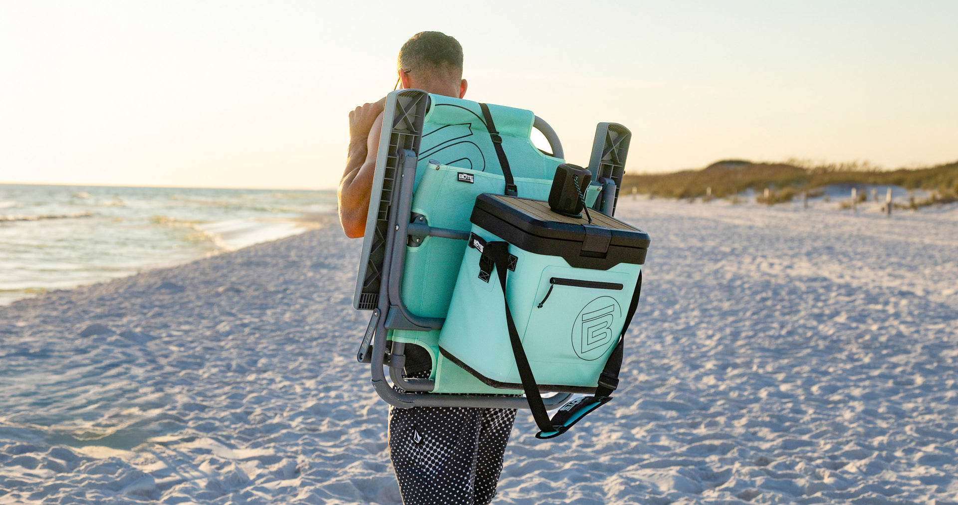 Person carrying KULA Mule cooler attached to beach chair on shoulder.