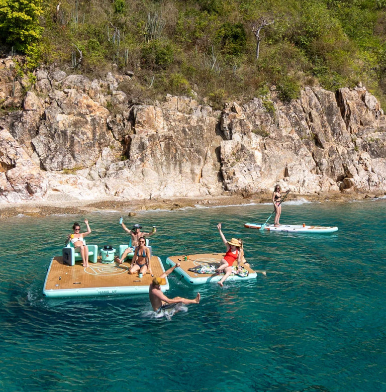 People enjoying activities on floating platforms and a paddleboard near rocky cliffs.