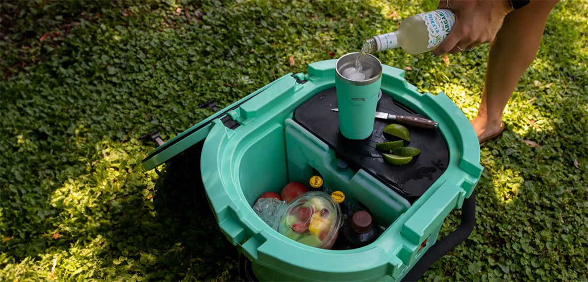 Open KULA 10 cooler filled with drinks and fruit while a drink is being poured over ice.