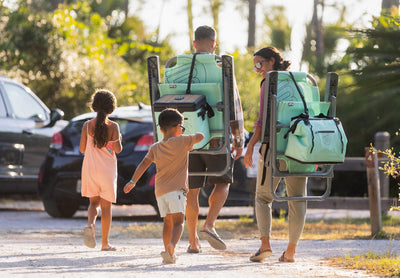 Family carrying Mule Outpost Chairs with attached cooler and bag on path.