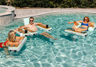 Three adults relaxing on inflatable pool loungers with cup holders.