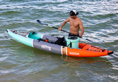 Side view of the Koda Aero with man holding a paddle, with a cooler mounted on the rear deck.