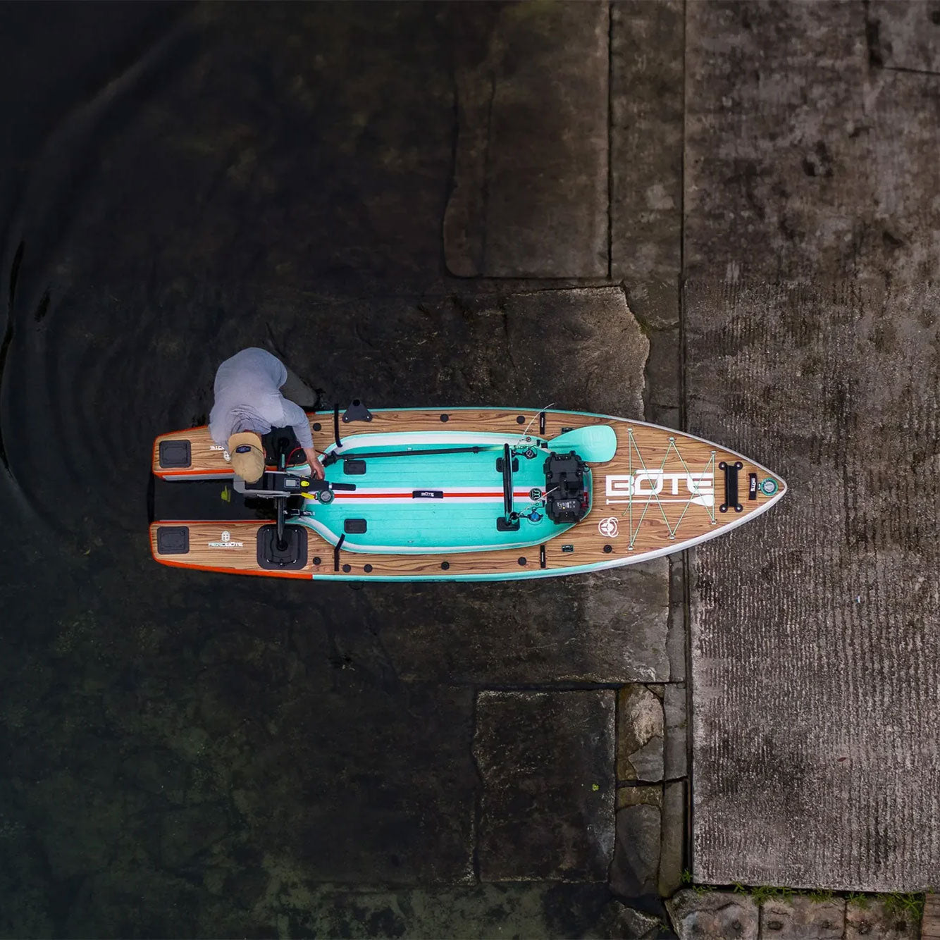 Top view of a person preparing the Rover Aero board with mounted motor at a concrete boat ramp.