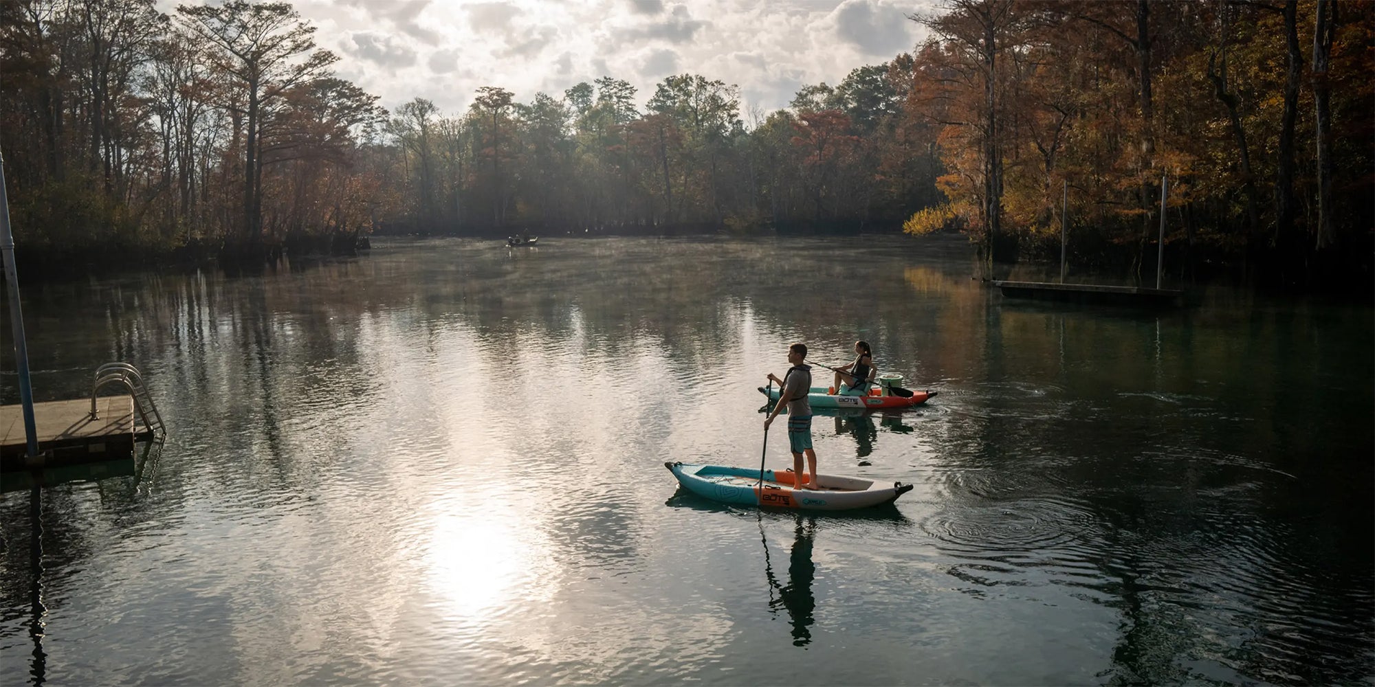 Two people paddling Zeppelin Aero kayaks on calm water surrounded by trees.