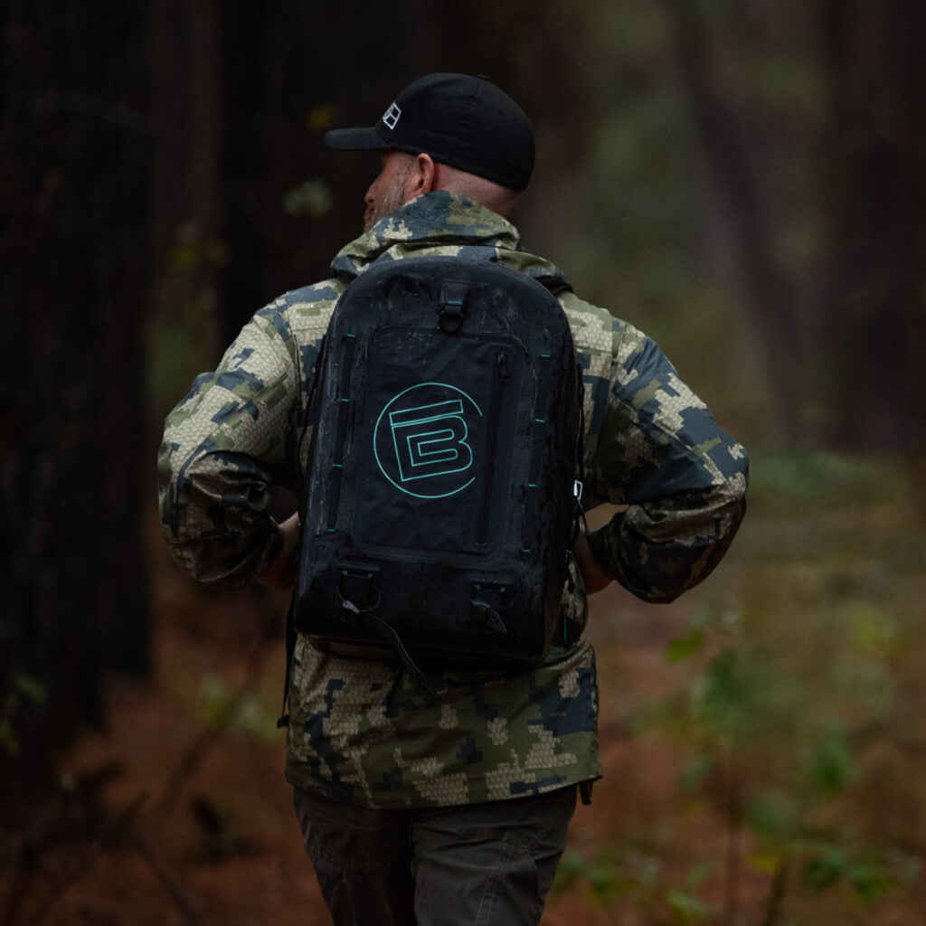 Man walking through the woods with the black Highwater Backpack on his back