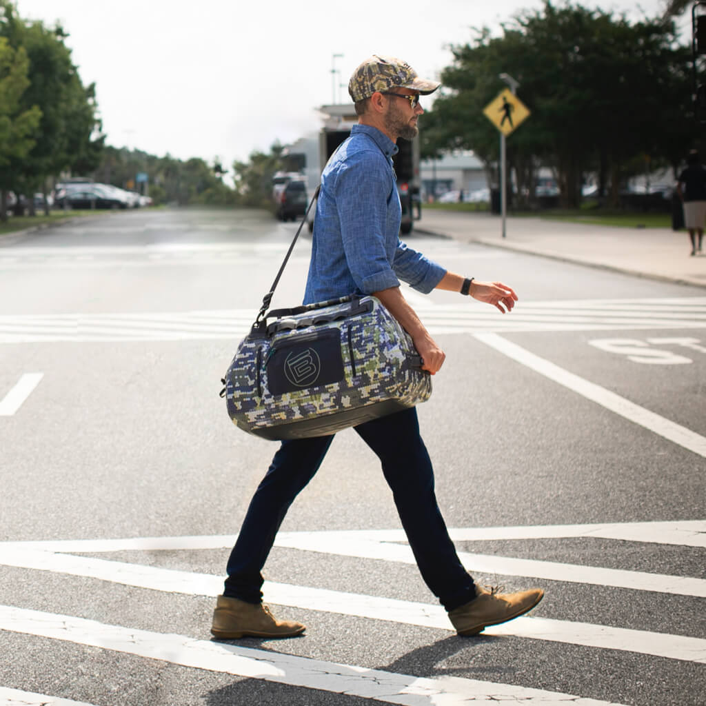 Man carrying Verge Camo Highwater Duffel over his shoulder as he walks across the street